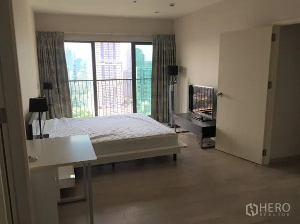 Condominium for rent in Khlong Toei, Bangkok - Master bedroom with large window, balcony and city view, plus TV console.