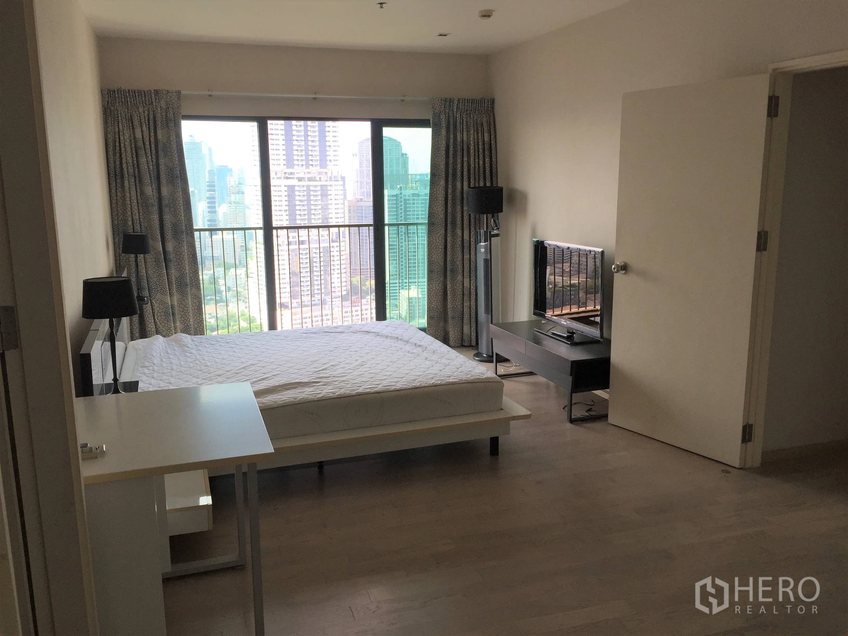 Condominium for rent in Khlong Toei, Bangkok - Master bedroom with large window, balcony and city view, plus TV console.