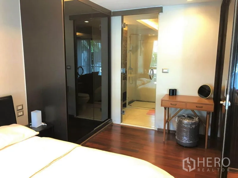 Condominium for rent in Watthana, Bangkok - Cozy bedroom with dark-glass wardrobe and an ensuite bathroom behind a clear shower screen.