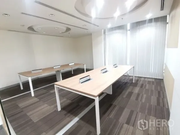Office Space for rent in Bang Rak, Bangkok - Carpeted team room with two long worktables and tall windows filtered by blinds.
