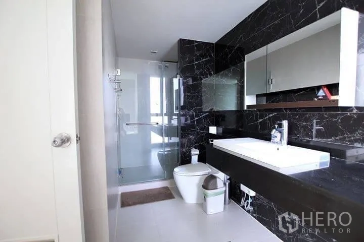 Condominium for rent in Watthana, Bangkok - Contemporary bathroom with black marble feature wall, wide vanity and glass-enclosed shower.