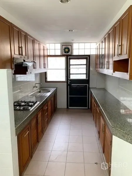 Detached House for rent in Khlong Toei, Bangkok - Galley kitchen featuring granite countertops, wooden cabinetry, gas hob and rear door.