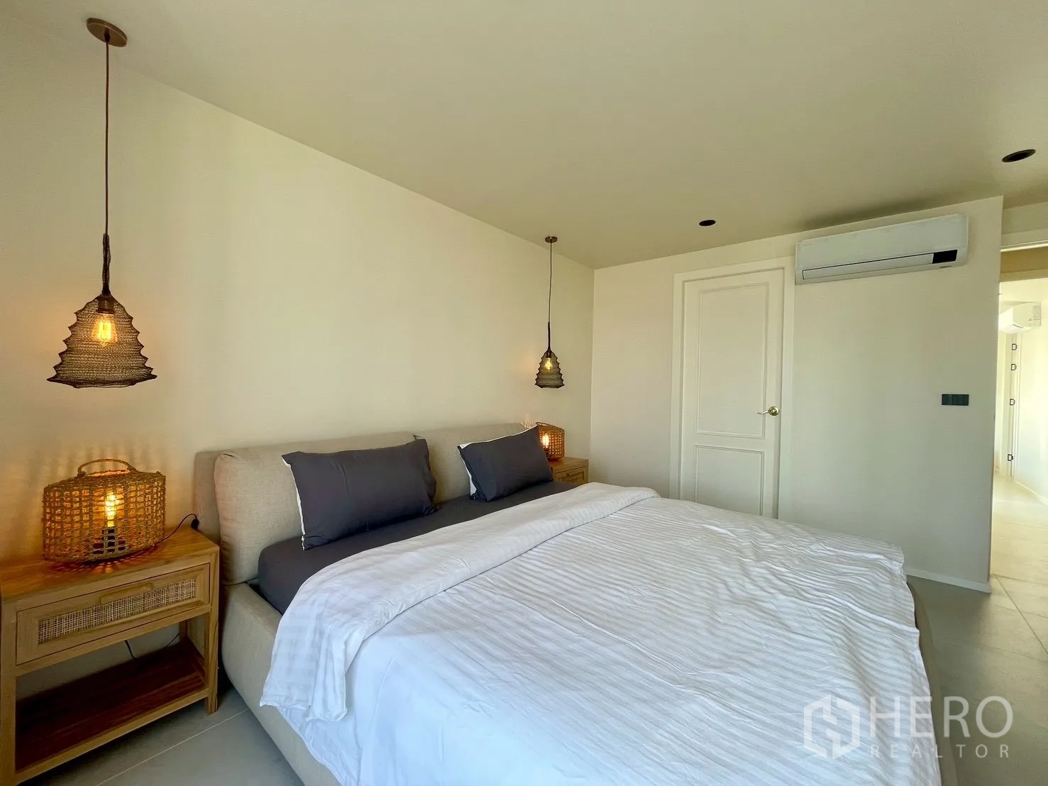 Condominium for sale in Watthana, Bangkok - Bedroom with woven pendant lamps, side tables, and air conditioner.