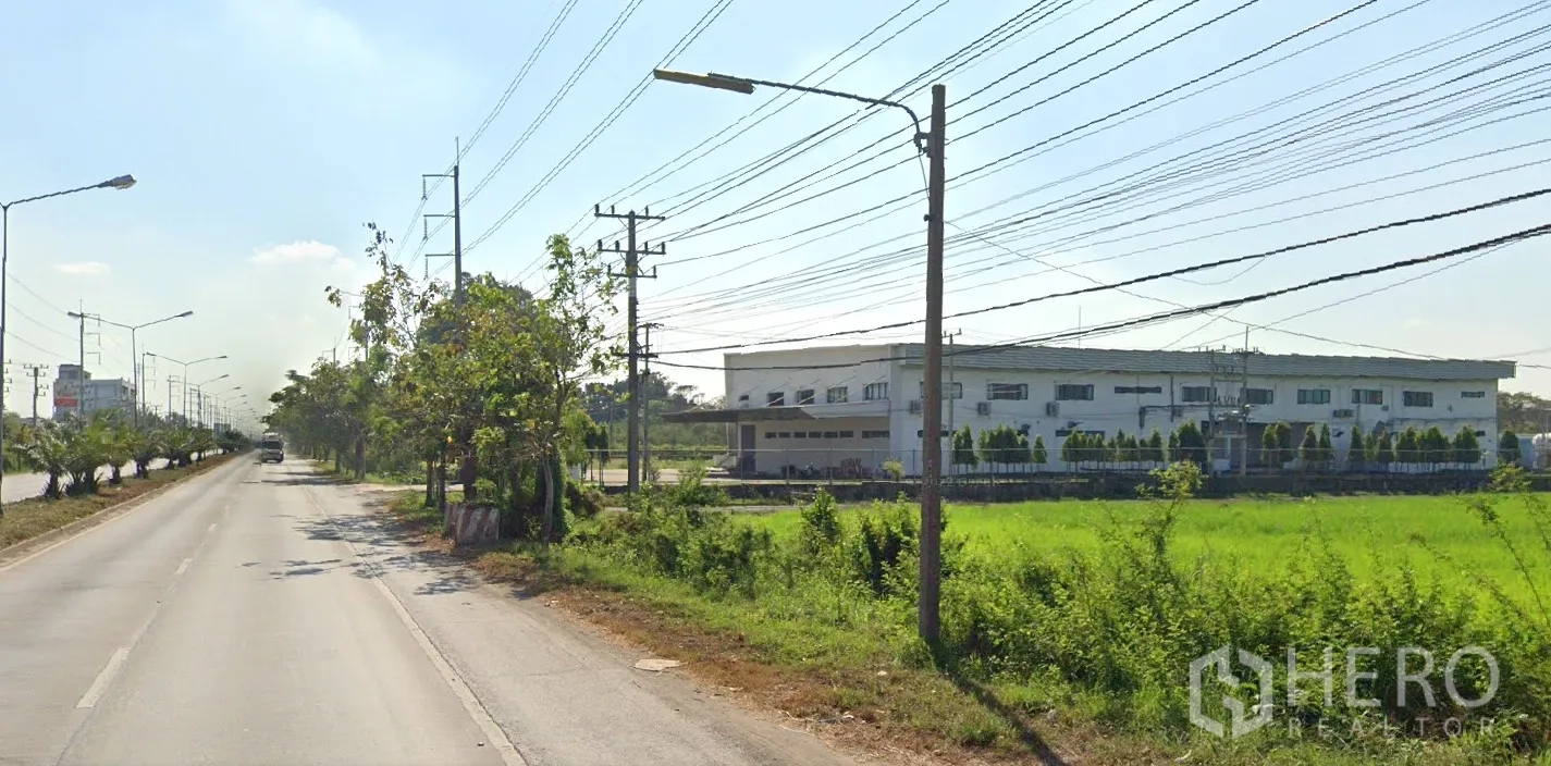 Land for sale in Lat Lum Kaeo, Pathum Thani - Roadside scene with a modern factory and green fields opposite the land along the main carriageway.