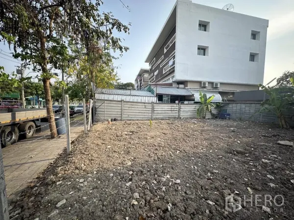 Land for sale in Saphan Sung, Bangkok - Level land inside boundary fencing next to low-rise residential and utility buildings.