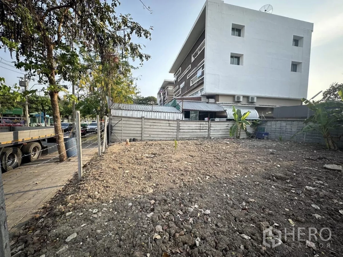 Land for sale in Saphan Sung, Bangkok - Level land inside boundary fencing next to low-rise residential and utility buildings.
