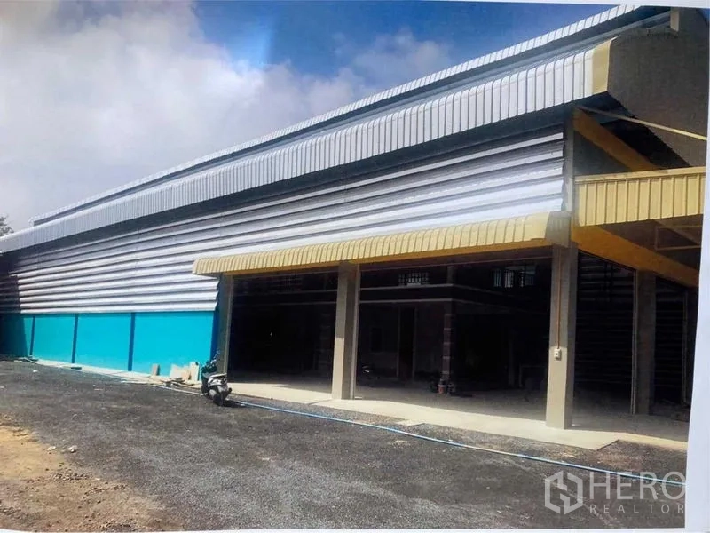 Warehouse for rent in Bang Pakong, Chachoengsao - Daytime exterior of metal-clad warehouse with yellow canopy and wide driveway.