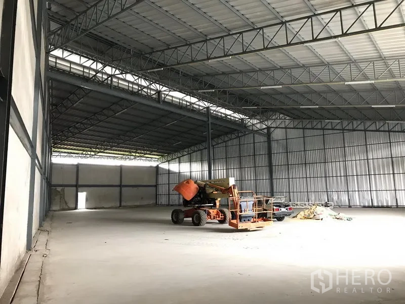 Warehouse for rent in Bang Phli, Samut Prakan - Open-plan warehouse hall with skylight strips, metal cladding walls, and equipment on the concrete floor.