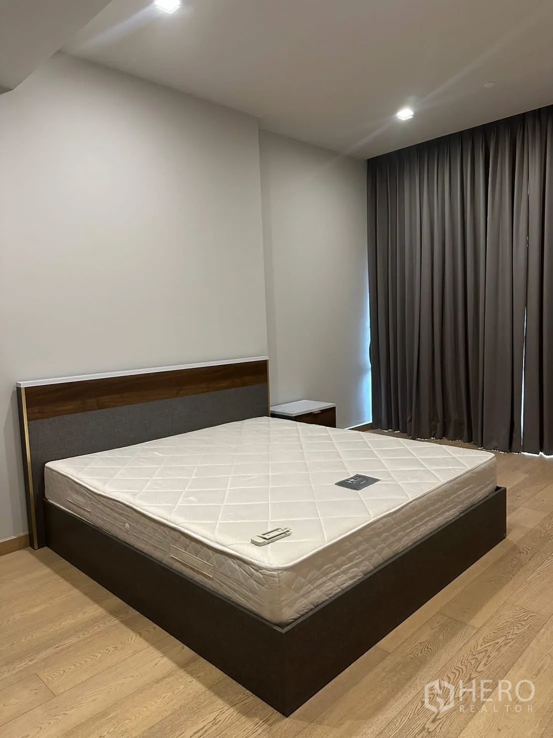 Condominium for rent or sale in Watthana, Bangkok - Guest bedroom with queen bed, wood floors, and blackout curtains.