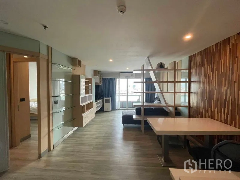 Condominium for rent in Sathon, Bangkok - Bright lounge and dining area with built-in TV wall, partition shelves and balcony doors opening to a city view.