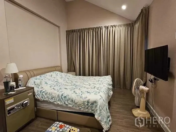 บ้าน ขายในBang Kruai, Nonthaburi - ห้องนอนเพดานสูง ผ้าม่านทึบ ทีวีติดผนัง และตู้ข้างเตียง