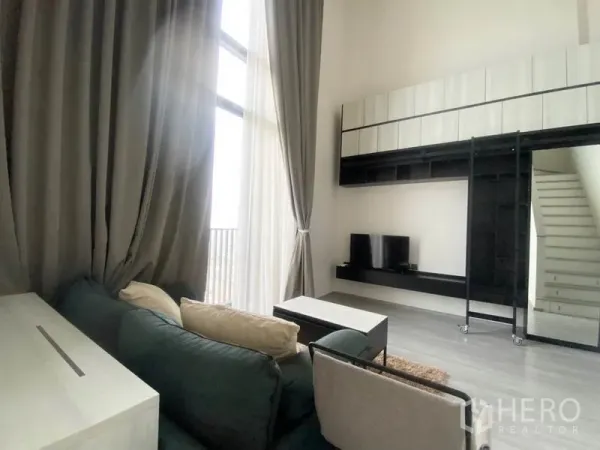 Condominium for rent in Phra Khanong, Bangkok - Double-height living area with built-in wall storage, TV console, large drapes and modern finishes.
