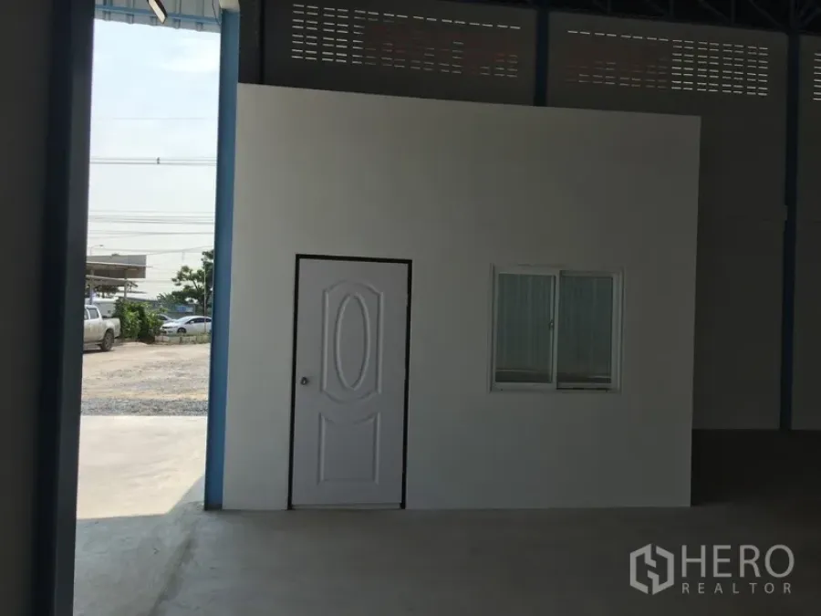 Factory for rent in Pathum Thani - Internal office with white door and window inside a high‑ceiling factory, adjacent to a driveway.