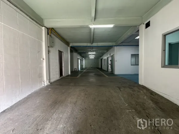 Warehouse for rent in Bang Na, Bangkok - Ground-floor warehouse aisle with concrete floor, fluorescent lights and partitioned rooms.