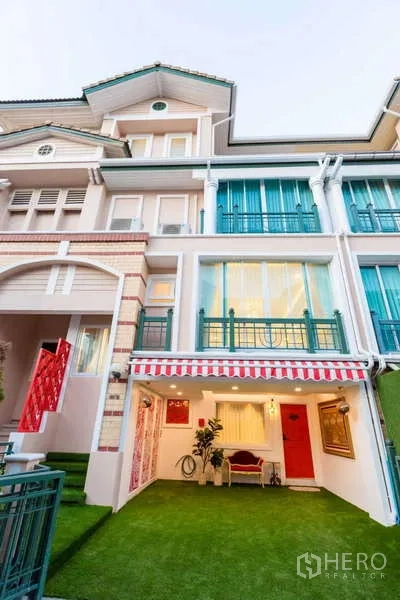 联排别墅 出租在Lat Phrao, Bangkok - 多层联排别墅外立面，带条纹遮阳篷、阳台栏杆和前庭草坪