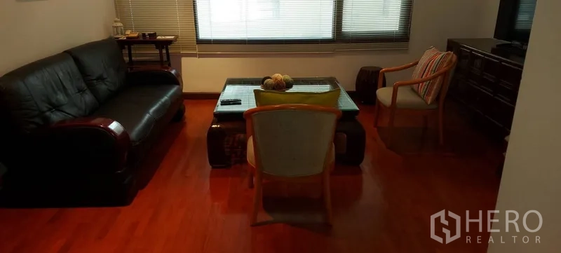 คอนโด ให้เช่าในSathon, Bangkok - ห้องนั่งเล่นอบอุ่น โซฟาหนังสีดำ โต๊ะกลางกระจก พื้นไม้ และบานหน้าต่างพร้อมมู่ลี่