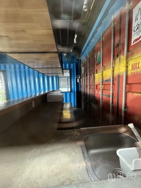 พื้นที่ขายปลีก ให้เช่า - โซนหลังร้าน มีอ่างล้างมือ เคาน์เตอร์ยาว และผนังตู้คอนเทนเนอร์