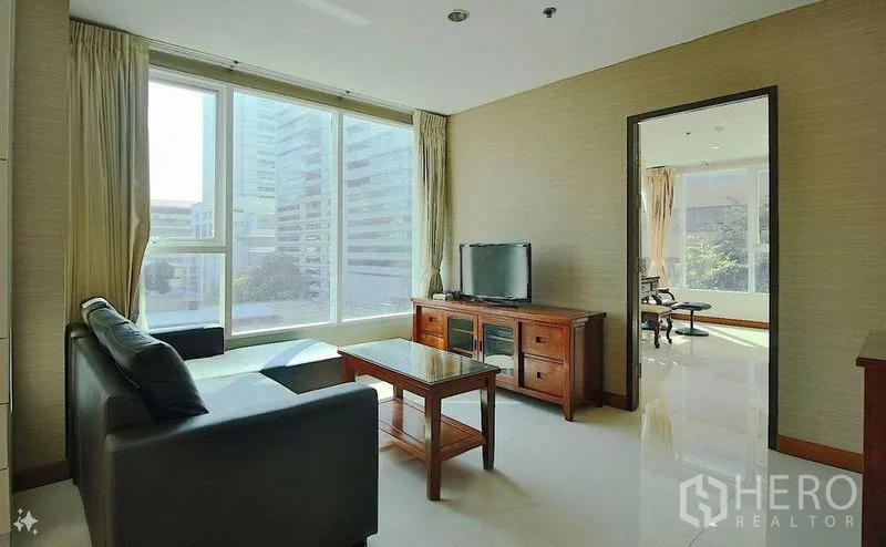 Condominium for sale in Watthana, Bangkok - Living area with TV console, sofa and floor-to-ceiling windows overlooking the Asok business district.