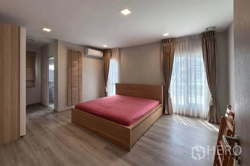 Semi-detached House for rent in Prawet, Bangkok - Spacious bedroom with wood floors, large windows, and door to a bathroom.