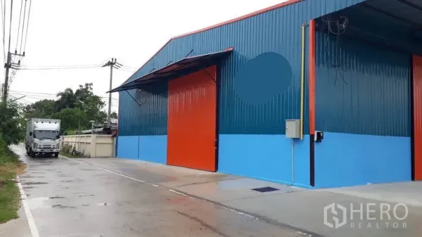 工厂 出租在Khlong Luang, Pathum Thani - 工厂临街外观，橙色大门，混凝土道路可供卡车通行。