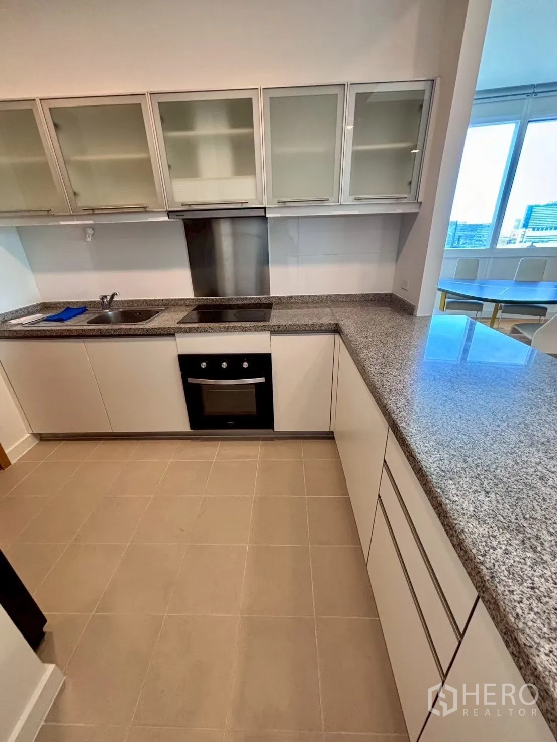 Condominium for rent in Khlong Toei, Bangkok - Modern kitchen with granite countertops, oven, cooktop and glass-front cabinets beside dining area