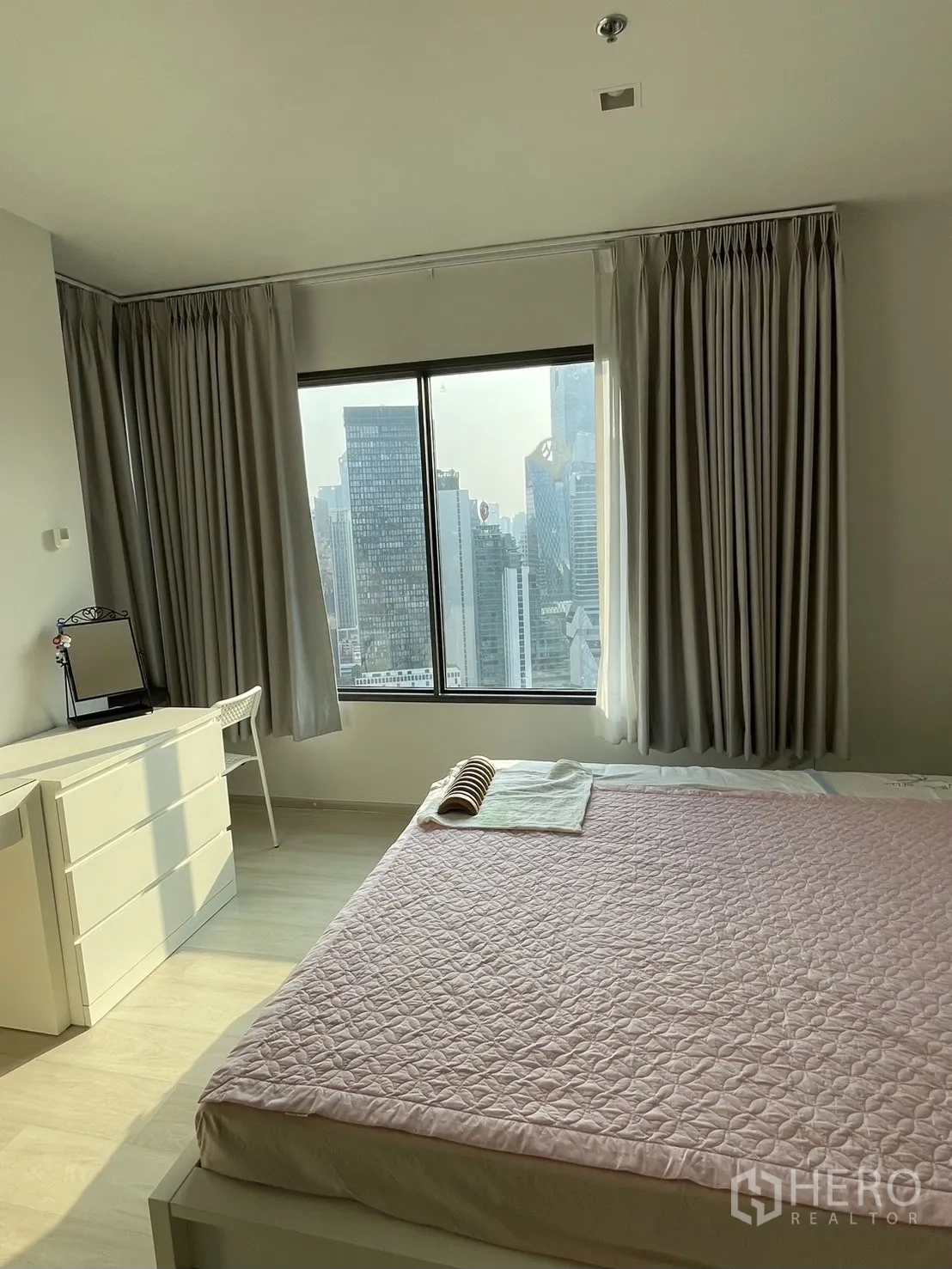 Condominium for rent in Pathum Wan, Bangkok - Spacious bedroom with large windows, pink quilted bed and dresser facing the city view.