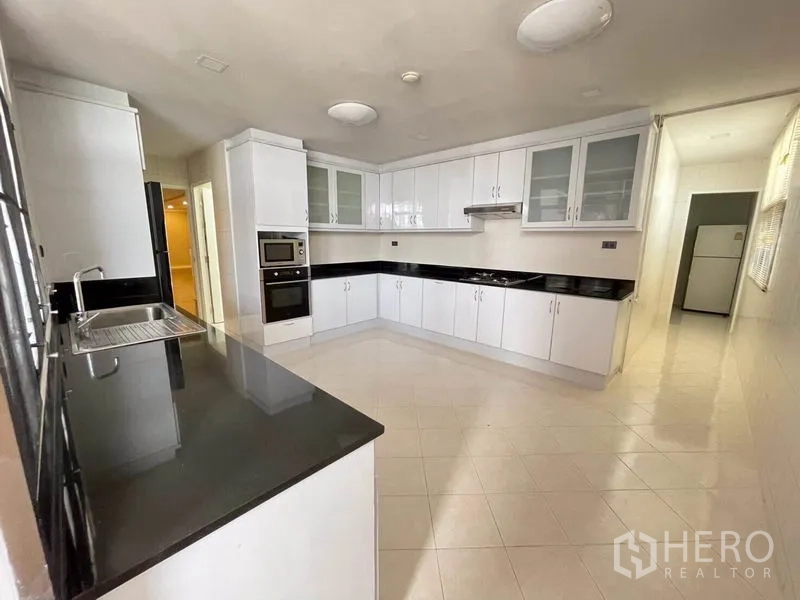 Condominium for rent in Watthana, Bangkok - Closed kitchen with white cabinetry, black granite countertops, and built-in oven.