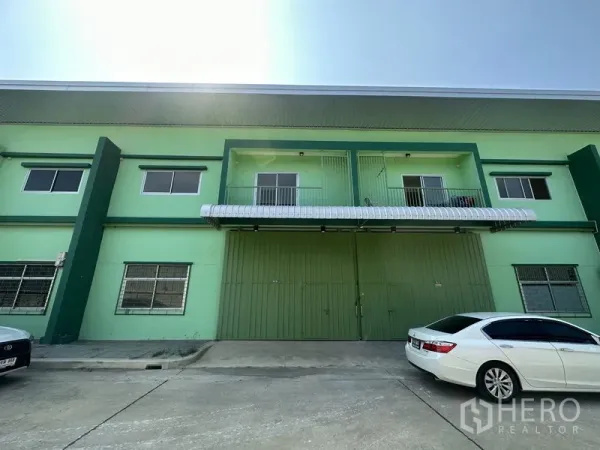 Warehouse for rent in Pathum Thani - Green two‑storey warehouse facade with large steel double doors and parking apron.