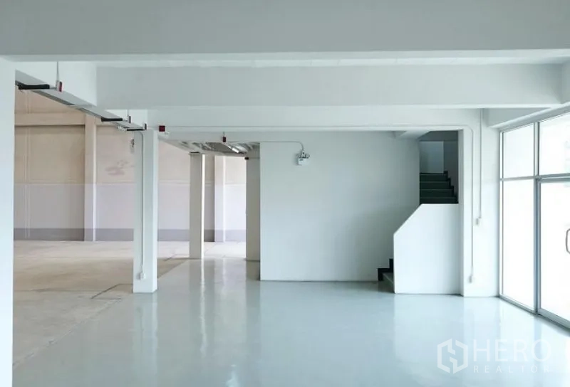 工厂 出租在Pluak Daeng, Rayong - 洁净的生产/包装区，环氧地坪、结构柱与临街玻璃立面旁的楼梯。