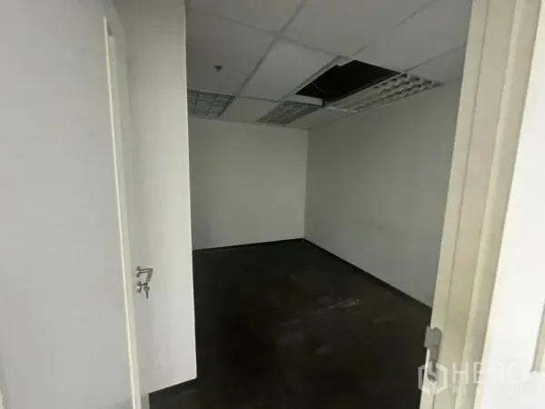 办公空间 出租在Khlong Toei, Bangkok - 小型空置办公室，深色地毯，格栅灯吊顶与开启的房门。