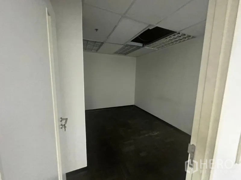 办公空间 出租在Khlong Toei, Bangkok - 小型空置办公室，深色地毯，格栅灯吊顶与开启的房门。