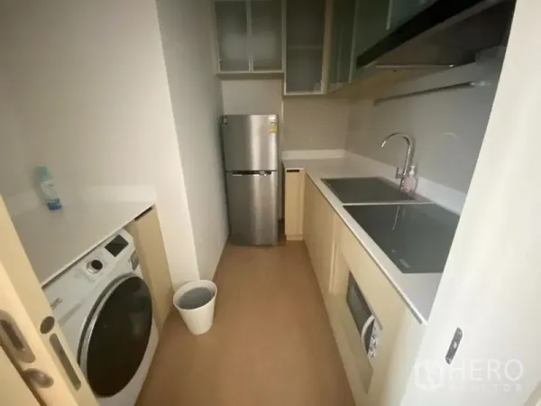 Condominium for rent in Watthana, Bangkok - Compact separate kitchen with induction hob, microwave, stainless fridge, washing machine, and white countertops.