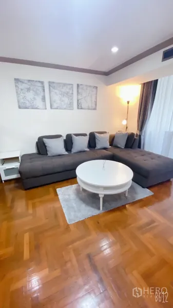 Condominium for rent in Watthana, Bangkok - Bright living room with a dark L-shaped sofa, white round coffee table, parquet floor, wall art and a floor lamp.