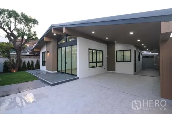 独立式住宅 出售在Bueng Kum, Bangkok - 现代单层独栋别墅外观，带遮棚车位、大窗户、铺砖车道与小草坪，傍晚灯光柔和