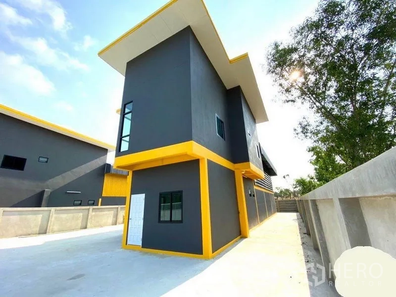Warehouse for rent in Lat Lum Kaeo, Pathum Thani - Side view of the warehouse-office building with secure concrete wall and wide driveway.