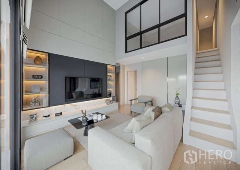 Condominium for rent in Huai Khwang, Bangkok - Living room with feature TV wall, illuminated shelves and staircase to mezzanine.