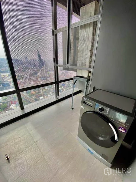 Condominium for rent in Sathon, Bangkok - High-rise utility balcony with washing machine and expansive Bangkok skyline view.