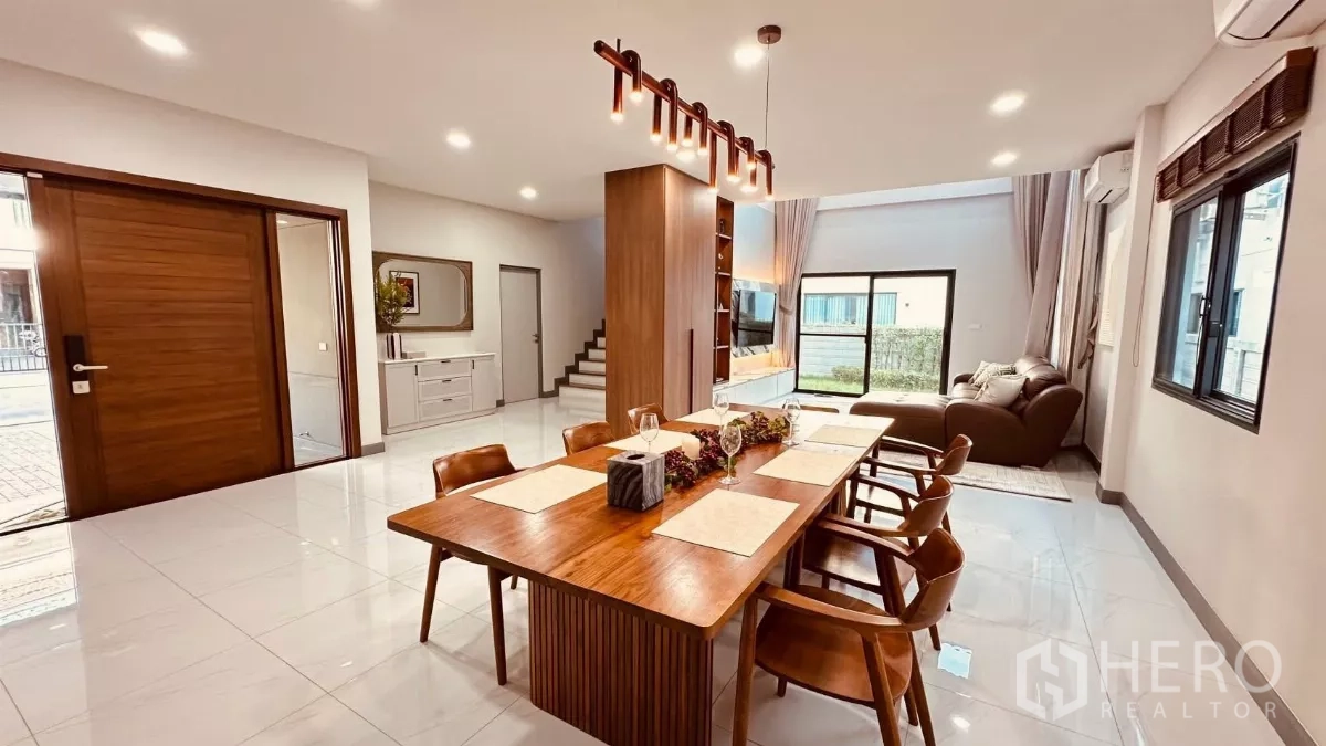 Detached House for rent in Bang Phli, Samut Prakan - Open‑plan dining and living area with a wooden table, pendant lights and sliding doors to the garden.
