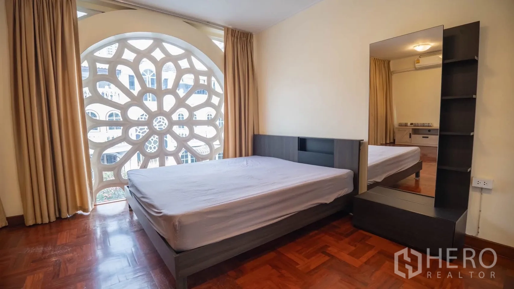 Townhouse for rent in Watthana, Bangkok - Bedroom with double bed and large arched decorative screen overlooking neighboring buildings.