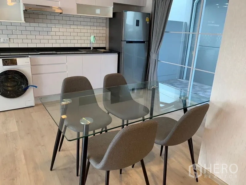 联排别墅 出租 - 四人玻璃餐桌紧邻厨房，旁有通向露台的落地门。