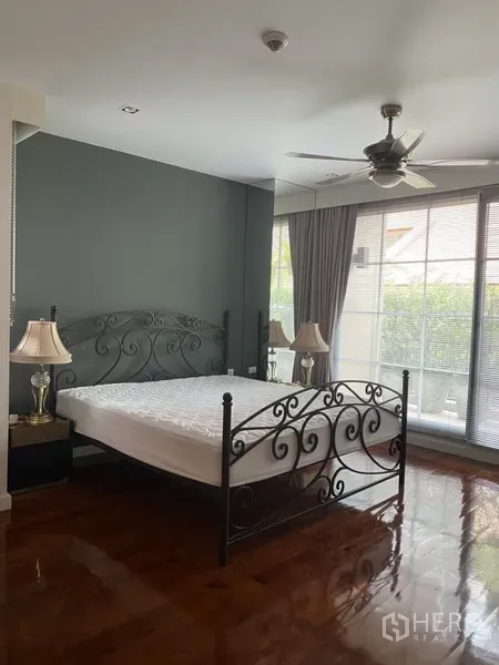 Apartment for rent in Pathum Wan, Bangkok - Primary bedroom with wrought-iron bed, ceiling fan and floor-to-ceiling windows with blinds.