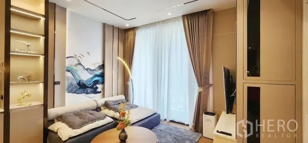 คอนโด ให้เช่า - ห้องนั่งเล่นอบอุ่น โซฟา ผนังทีวี และผ้าม่านโปร่งสู่ระเบียง