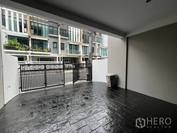 ทาวน์เฮาส์ ให้เช่าหรือขายในKhlong Toei, Bangkok - ที่จอดรถมีหลังคาพร้อมประตูเหล็ก พื้นคอนกรีตพิมพ์ลาย มองออกไปยังทาวน์โฮมฝั่งตรงข้าม