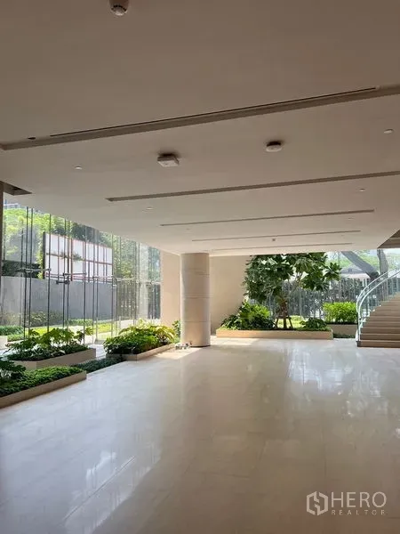 零售空间 出租 - 明亮的零售大堂，大窗、嵌入式顶灯、绿化花槽，旁有弧形楼梯与圆形立柱。