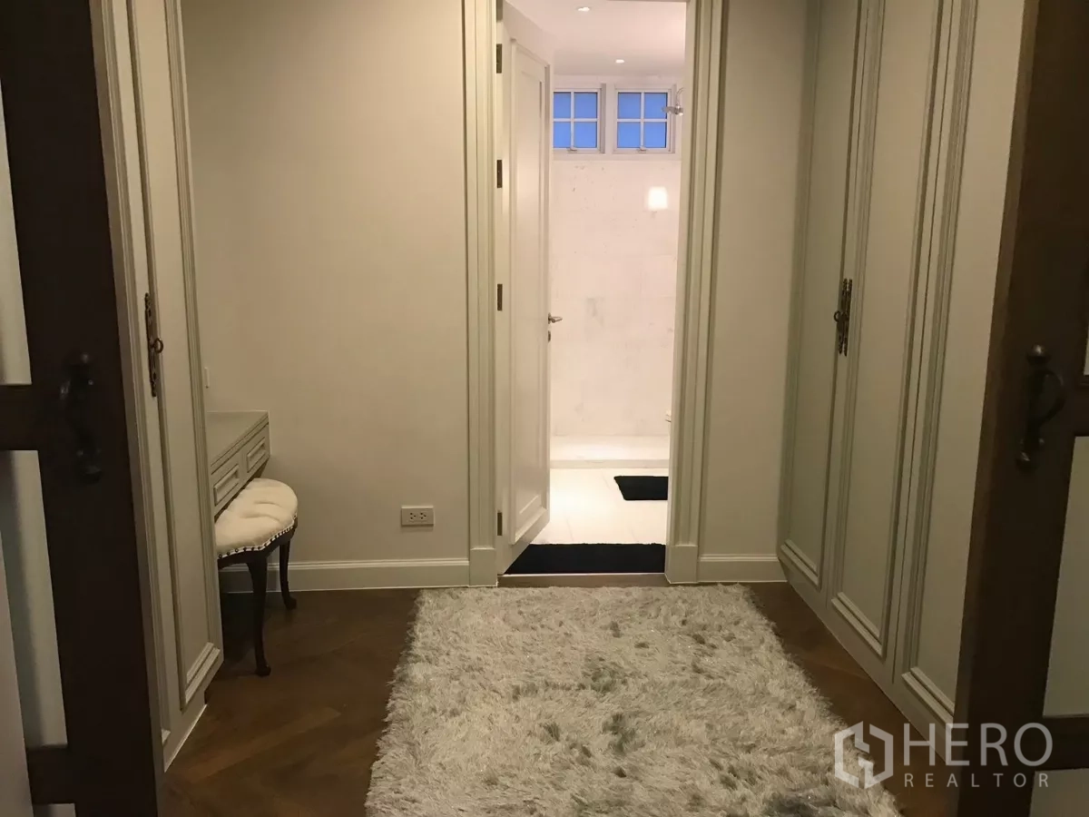 Townhouse for sale in Watthana, Bangkok - Hallway with wardrobes and shag rug leading to a light marble bathroom.