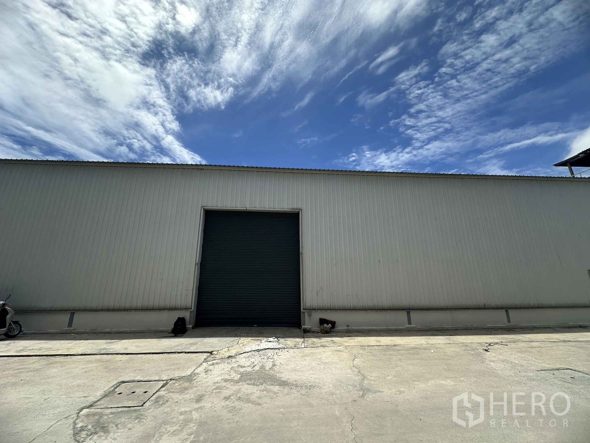 โรงงาน for rent in Mueang Samut Prakan, Samut Prakan - อาคารโรงงานผนังเมทัลชีทพร้อมประตูม้วนขนาดใหญ่และลานคอนกรีตใต้ท้องฟ้าสีคราม