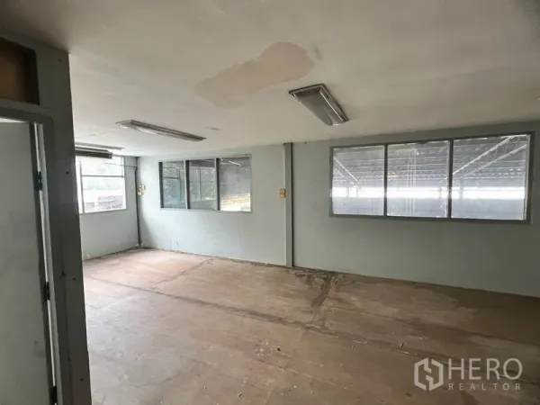 Warehouse for rent in Suan Luang, Bangkok - Empty office room inside the warehouse with windows, fluorescent lights, and wooden flooring panels.