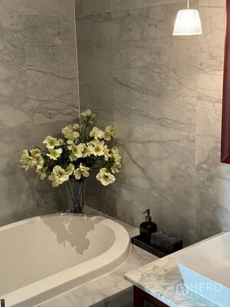 Condominium for sale in Watthana, Bangkok - Detail of marble-clad bathtub corner with a vase of white flowers.
