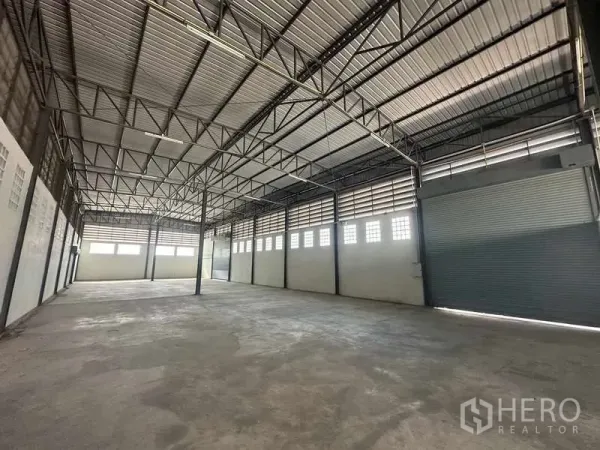 货栈 出租在Bang Bua Thong, Nonthaburi - 仓库内部空间开阔，高钢结构屋顶与卷闸门