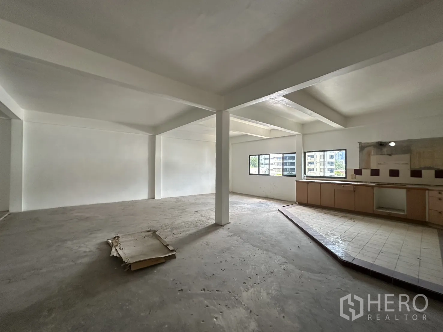 零售空间 for rent in Watthana, Bangkok - 开放式零售楼层，白色墙面与立柱，多扇窗户，带抬高瓷砖区和内置柜台。